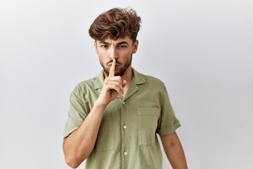 Young arab doctor man standing over isolated background asking to be quiet with finger on lips. silence and secret concept.