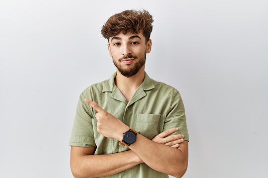 Young arab doctor man standing over isolated background pointing with hand finger to the side showing advertisement, serious and calm face