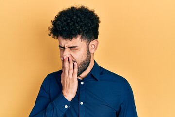 Young arab man with beard wearing casual shirt bored yawning tired covering mouth with hand. restless and sleepiness.