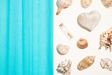 Message in a bottle with sea shells, heart shape and blue crepe paper on beige background. Summer, vacation Love or Valentine's Day concept. Flat lay.