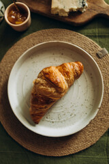 Fresh croissant on a white ceramic plate on a woven set. Baked croissant top view.