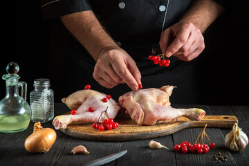 Professional cook prepares raw chicken legs in the kitchen. The chef puts the red viburnum on the chicken leg before baking. National dish.