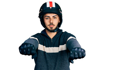 Young hispanic man with beard wearing motorcycle helmet doing driving gesture relaxed with serious...