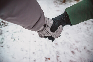 The couple holds hands in mittens walking in the snowy winter forest