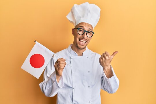 Bald Man With Beard Wearing Professional Cook Uniform Holding Japan Flag Pointing Thumb Up To The Side Smiling Happy With Open Mouth