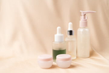 Jars of serum with a dropper for moisturizing the skin of the face, two jars of day and night cream on a nude creamy silk fabric. Skin care.