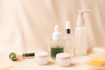 Jars of serum with a dropper for moisturizing the skin of the face, two jars of day and night cream on a nude creamy silk fabric. Skin care.