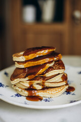 Stack of pancakes on a plate close-up. Maple syrup flows from a stack of pancakes. Pancakes with maple syrup