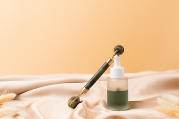 Facial serum and roller massager on nude pink silk fabric. Skin care.
