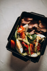 healthy varied food in a paper plate on a white background. a portion of hot salad with boiled eggs and chopped veal. food delivery and takeaway top view. sports nutrition for muscles and weight loss