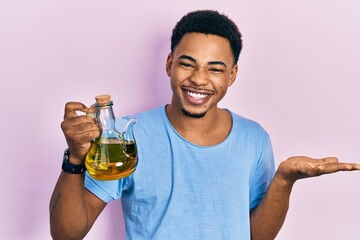 Young african american man holding olive oil can celebrating achievement with happy smile and winner expression with raised hand