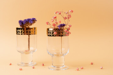 Two beautiful glass goblets with golden rims and flowers inside on nude cream fabric