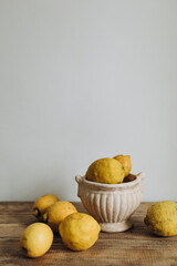 yellow organic lemons in a ceramic pot on a wooden table. ribbed lemons in a vintage bowl near a white wall. fresh whole raw lemons and place for text.