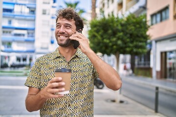 Young hispanic man talking on the smartphone drinking coffee at street