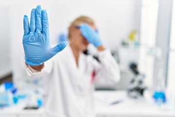 Middle age blonde woman working at scientist laboratory covering eyes with hands and doing stop gesture with sad and fear expression. embarrassed and negative concept.