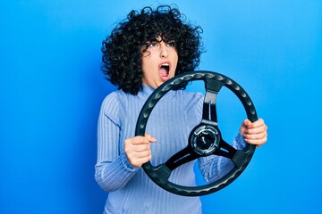 Young middle east woman holding steering wheel angry and mad screaming frustrated and furious,...