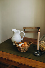 white and brown eggs in a wicker bowl on the kitchen table. raw whole homemade eggs in a bowl on the table with a burning candle.