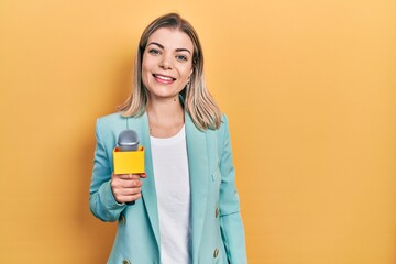 Beautiful caucasian woman holding reporter microphone looking positive and happy standing and...