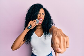 Middle age african american woman singing song using microphone pointing with finger angry and mad...