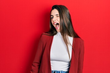Young brunette teenager wearing business jacket winking looking at the camera with sexy expression,...