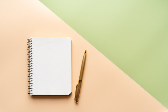 Background of two colors, light green and peach. Top view, wallpaper. Notebook and golden pen.