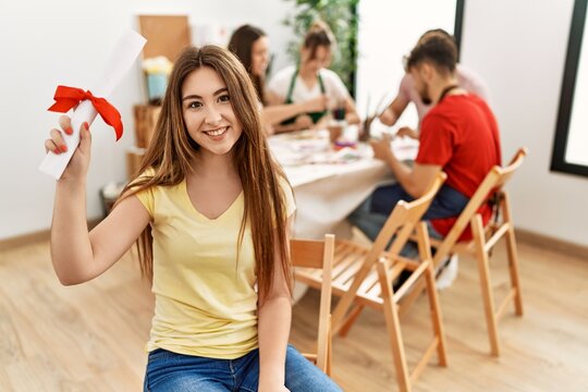 Group of people drawing sitting on the table. Young woman smiling happy holding diploma at art studio.