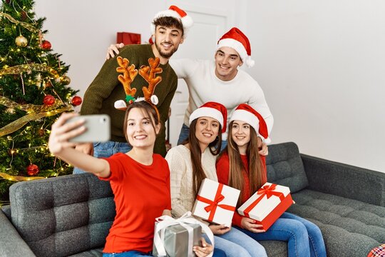 Group of young people holding christmas gifts make selfie by the smartphone at home.