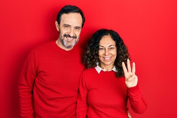 Middle age couple of hispanic woman and man hugging and standing together showing and pointing up with fingers number three while smiling confident and happy.