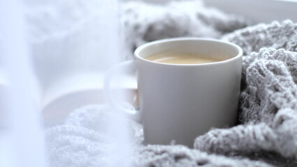 Cozy home with cup of coffee and a book. Hygge style. Mug of black coffee wrapped in warm scarf on...