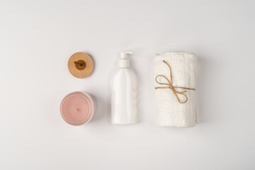 Flatlay, bottle of shampoo, candle in glass jar and towel on white background.