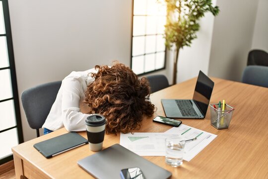 Middle age hispanic woman overworked with head on table at office