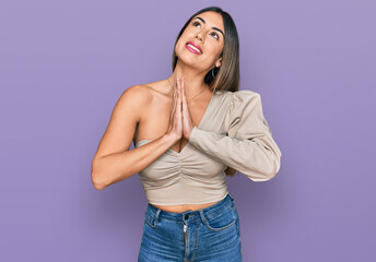 Young hispanic woman wearing casual clothes begging and praying with hands together with hope...