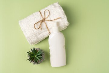 A white bottle of shampoo or lotion, a clean fresh towel and an indoor ornamental plant on a light green background. Beauty and care for hair and body.