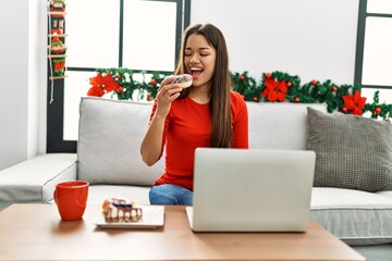 Young latin woman having breakfast using laptop sitting by christmas decor at home