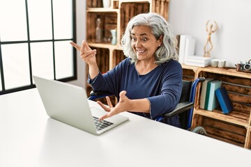 Middle age grey-haired disabled woman having video call sitting on wheelchair at home.