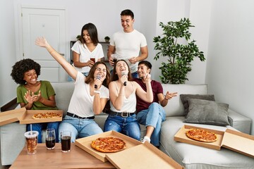 Group of young friends having party eating italian pizza and singing song at home.