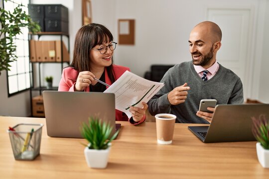 Two hispanic business workers smiling happy working using laptop and smartphone at the office.