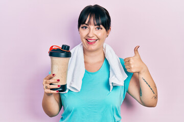 Young hispanic woman wearing sport clothes drinking a protein shake smiling happy and positive,...