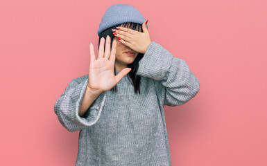 Young hispanic woman wearing cute wool cap covering eyes with hands and doing stop gesture with sad and fear expression. embarrassed and negative concept.