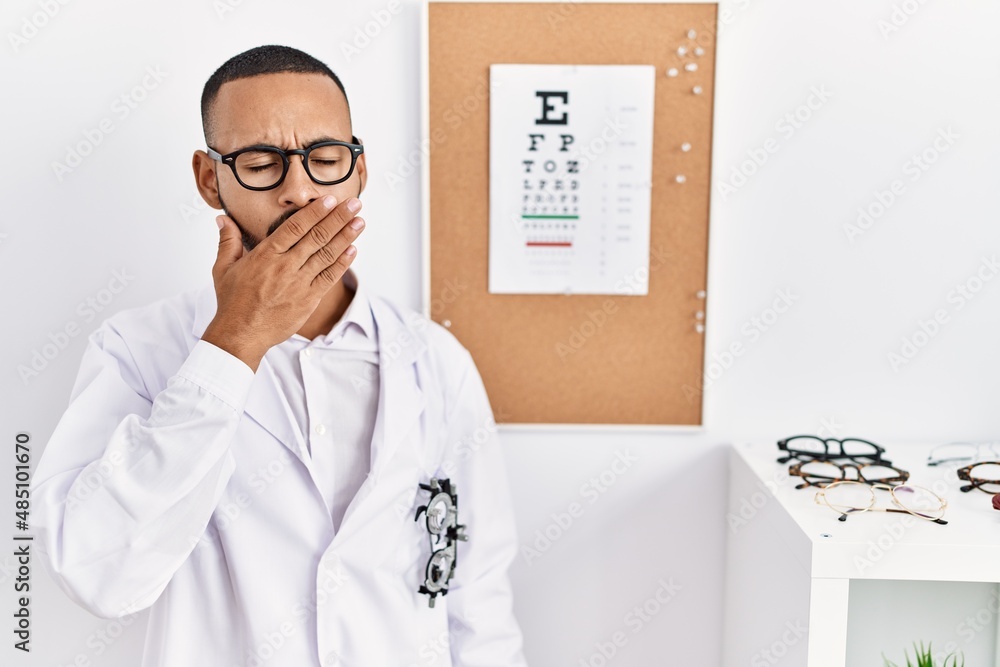 Sticker African american optician man standing by eyesight test bored yawning tired covering mouth with hand. restless and sleepiness.