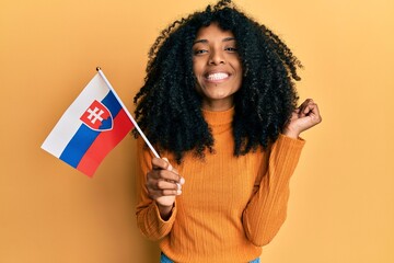 African american woman with afro hair holding slovakia flag screaming proud, celebrating victory and success very excited with raised arm