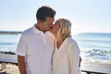 Middle age man and woman couple hugging each other and kissing standing at seaside