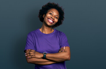 African american woman with afro hair wearing casual purple t shirt happy face smiling with crossed...