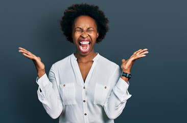 African american woman with afro hair wearing casual white t shirt celebrating mad and crazy for success with arms raised and closed eyes screaming excited. winner concept