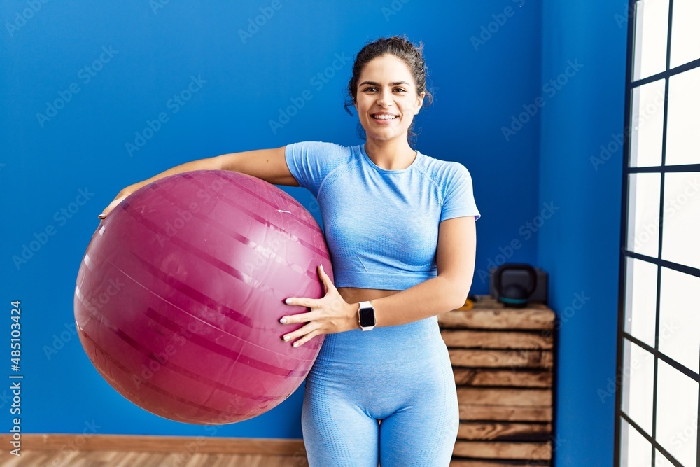 Wall mural young latin woman wearing sportswear holding fit ball at sport center - Wall murals