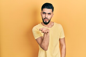 Handsome man with beard wearing casual yellow t shirt looking at the camera blowing a kiss with...