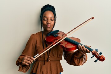 African american woman with braided hair playing violin looking at the camera blowing a kiss being...