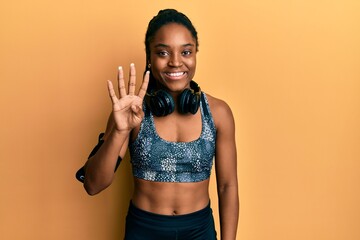African american woman with braided hair wearing sportswear and arm band showing and pointing up with fingers number four while smiling confident and happy.