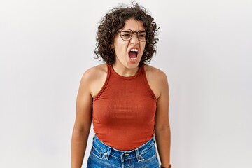 Young hispanic woman wearing glasses standing over isolated background angry and mad screaming...