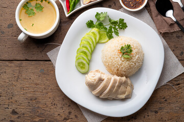 Sliced Hainan-style chicken with marinated rice served with chilli sauce and cucumber in white plate.Asian food style